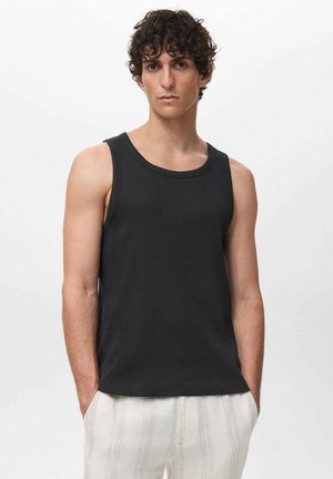 Débardeur noir à côtes avec un col rond, à manches sans épaules et coupe ajustée, porté avec un pantalon rayé de couleur claire.