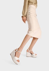 Sandali wedge bianchi con design a punta aperta e cinturino alla caviglia, caratterizzati da una texture liscia e una robusta piattaforma per un'altezza extra.