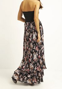 Vestido maxi con un corsé negro sin tirantes y una falda floral plisada en negro, rosa y crema, con volantes en capas en el dobladillo.