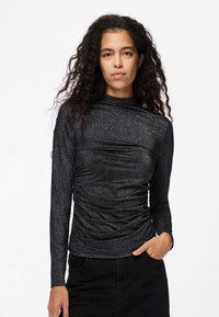 Svart långärmad topp med en glittrig textur, med hög hals och rynkade detaljer vid midjan. Bärs med en svart kjol.