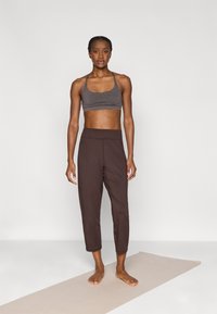 Αθλητική εμφάνιση με αθλητικό σουτιέν σε γκρι μελανζέ και σκούρες καφέ cropped παντελόνες, και τα δύο κατασκευασμένα από ελαφρύ, ελαστικό ύφασμα.