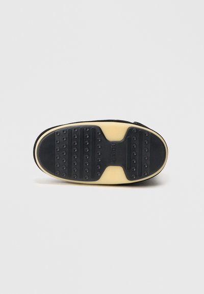 Semelle de chaussure en caoutchouc noir avec une surface texturée présentant des motifs de grip ronds, une semelle intermédiaire de couleur crème contrastante et un bout lisse et arrondi.