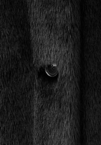 Tejido de piel sintética negra con una apariencia densa y texturizada. Presenta un botón redondo negro parcialmente visible entre el pelo.