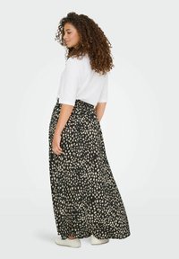Gonna maxi nera con macchie astratte bianche, tessuto fluido, vita elastica, abbinata a una maglietta bianca a maniche corte e scarpe bianche.