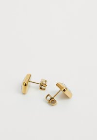Boucles d'oreilles en argent doré présentant un design rond lisse avec des accents de pierre transparente, sécurisées par une fermeture à poussoir.