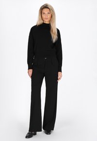 Pulover negru tricotat cu guler înalt, asortat cu pantaloni negri cu croi larg. Ținuta prezintă un material texturat și o siluetă elegantă.