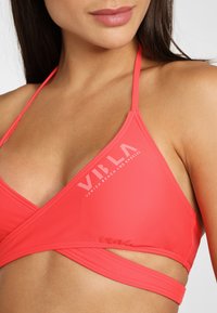 Haut de bikini corail avec un design enveloppant, fabriqué en tissu lisse, arborant un logo imprimé blanc "VILA" et des coutures accentuées.