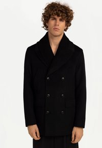 Svart ullpeacoat med sjalkrage, dubbelknäppt knäppning och två framfickor. Slät textur och skräddarsydd passform.