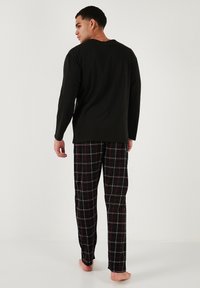 Cămașă neagră cu mânecă lungă asociată cu pantaloni de pijama în carouri negre și roșii, având o croială lejeră și un material moale.