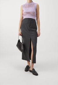 Violetti ilmanhihainen neulepaita, jossa on vaakasuorat kuviot, yhdistettynä tummanharmaaseen hameeseen, jossa on etureikä. Malli pitää mustaa laukkua.