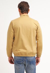 Khaki letvægtsjakke med en glat tekstur, elastiske cuffs og en tætsiddende talje, med et enkelt design uden synlige logoer.