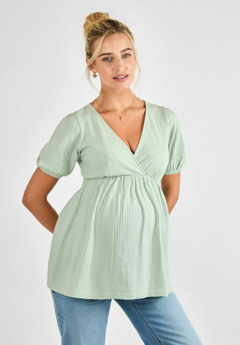 Világos zöld kismama blúz V-kivágással, rövid puff ujjakkal és emelkedett derékkal. Puha, textúrált anyag finom függőleges bordázattal.