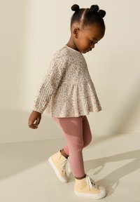 Camiseta de manga larga con estampado floral en tonos crema y rosa, combinada con leggings rosa suave y zapatillas altas amarillas con suelas blancas.