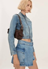 Modra denim jakna in krilo v svetli modri barvi, z obrezanim dizajnom, zadrgo in sprednjimi žepi; v kombinaciji z rjavim mini nahrbtnikom.