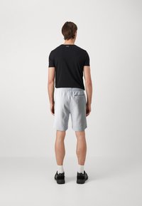 Schwarzes Kurzarm-T-Shirt und hellblaue Sportshorts mit elastischem Bund, ausgestattet mit einer Gesäßtasche. Das Modell trägt schwarze Turnschuhe mit weißen Socken.