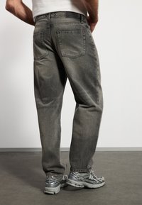 Gray denim jeans with a relaxed fit, featuring two back pockets and slight fading. Paired with silver athletic shoes and a plain white shirt.