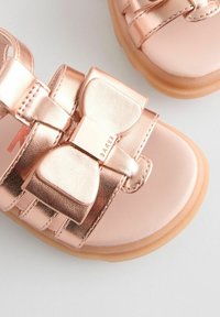 Roze gouden sandalen met een grote strikaccent, metallic afwerking, glad synthetisch bovenwerk en een flexibele, getextureerde tan zool.