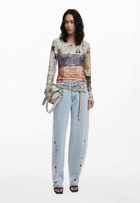 Långärmad skjorta med flerfärgade tryck; kombinerad med ljusblå vida jeans med knappar längs sidorna. Accessoarer med en liten väska.