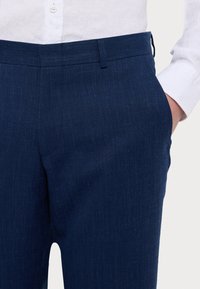Mörkblå linneblandade byxor med rak passform, med flat front och sidofickor, kombinerat med en vit skjorta med knappar.