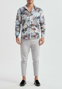 Chemise à boutons avec un motif floral en bleu, blanc et marron, associée à un pantalon tapered gris clair et des mocassins noirs.