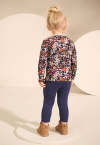 Bluză florală cu mâneci lungi, de culoare bleumarin închis, cu modele multicolore, combinată cu colanți bleumarin și ghete maro deschis până la gleznă.