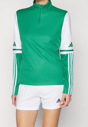 Grünes, weißes und dunkelgrünes Adidas Langarm-Sportshirt mit Viertel-Reißverschluss kombiniert mit weißen Adidas Shorts mit Logo am linken Bein.