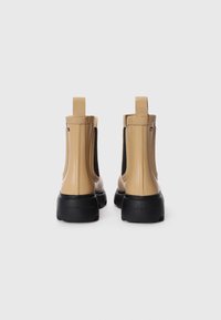 Stivaletti alla caviglia in gomma beige con pannelli elastici laterali, linguette e suole nere texturizzate. Finitura liscia con un marchio discreto sul lato.