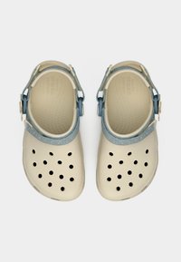 Crocs beiges avec des sangles réglables texturées bleues, des trous de ventilation sur le dessus et des semelles intérieures texturées, vus de dessus sur un fond uni.