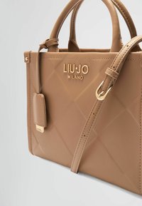 Bolso de mano de cuero marrón claro con un diseño acolchado, logo en tono dorado y correa de hombro desmontable. Presenta asas en la parte superior y una forma rectangular.
