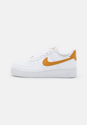 Biały sneaker typu low-top z pomarańczowym logo Nike swoosh i detalem na pięcie, białymi sznurówkami i teksturowaną podeszwą na jednolitym tle.