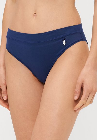 Tumšzilas kokvilnas bikini apakšdaļa ar vidēja augstuma jostasvietu, kreisajā pusē rotāta ar baltu izšūtu logo. Gluda, elastīga tekstūra.