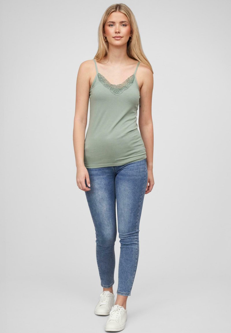 Mintgrønn camiskjorte med blondekant ved utringingen, parret med blå skinny jeans og hvite joggesko. Glatt stoff og tettsittende design.