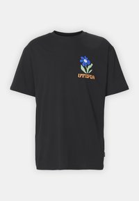 Camiseta de algodón negra con un gráfico de una flor azul y hojas verdes, y "UTERPA" en texto naranja en la parte delantera. Corte regular y mangas cortas.