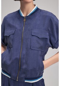 Granatowa kurtka bomberka z zapięciem na zamek, krótkimi rękawami, dwiema kieszeniami na piersi, elastycznym pasem z niebieskimi i białymi paskami.