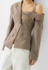 Blazer marron à rayures verticales avec un design décolleté et une fermeture à un bouton, associé à un jean clair taille haute.