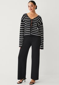 Zwart-wit gestreepte cardigan met een striksluiting, gecombineerd met zwarte textuur wijde broek en zwarte bandjeshakken.