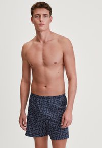 Pantaloni da bagno blu navy con motivi a spirale bianchi e rossi, vita elastica, realizzati in tessuto traspirante, taglio fino al ginocchio.