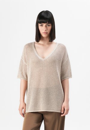 Lys beige strikkegenser med løs passform, V-hals og korte ermer, med en teksturert, åpen vevdesign. Kombinert med brune bukser.