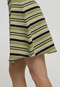 Jupe en tricot à rayures alternées vert, noir et beige. Tissu texturé avec un ourlet évasé et des coutures visibles.
