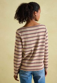 Beige Langarmshirt mit horizontalen weinrot und marineblauen Streifen, Rundhalsausschnitt und weichem Material. Mit einem Logo-Patch am Ärmel.