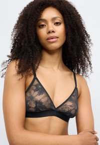 Μαύρο κορμάκι από δαντέλα με λουλουδάτο μοτίβο, τριγωνικά cups και ρυθμιζόμενους ιμάντες. Η κάτω ζώνη φέρει το λογότυπο "Tommy Hilfiger".