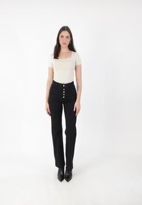 Top ajustado de color beige claro con escote cuadrado, combinado con pantalones negros de cintura alta con cierre de botones. Tacones negros de punta.