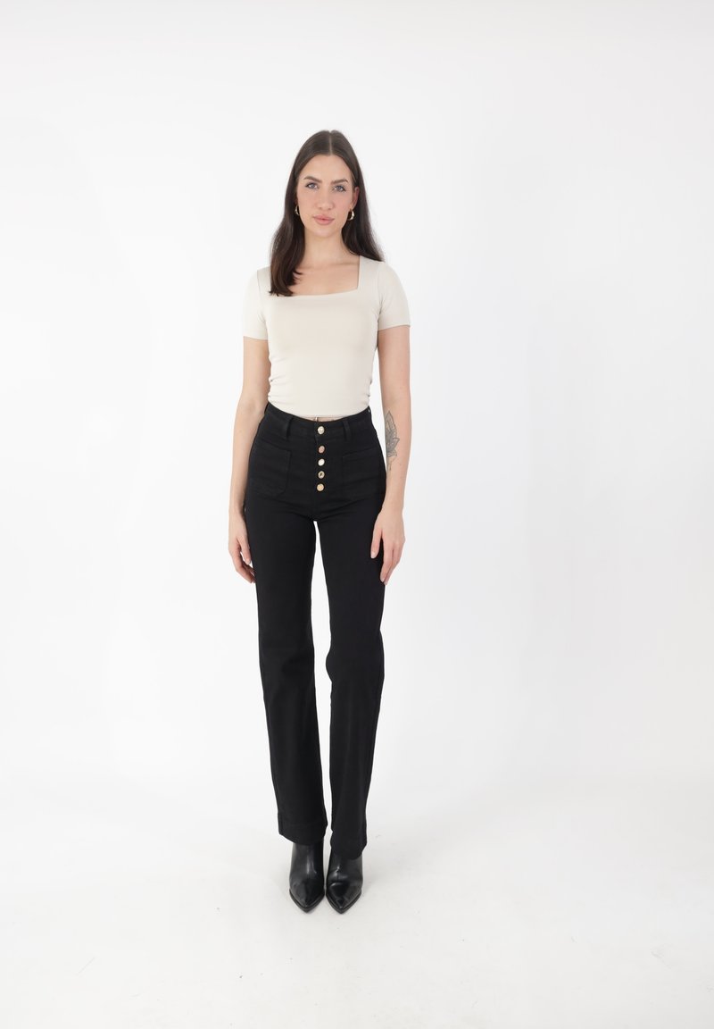 Top ajustado de color beige claro con escote cuadrado, combinado con pantalones negros de cintura alta con cierre de botones. Tacones negros de punta.