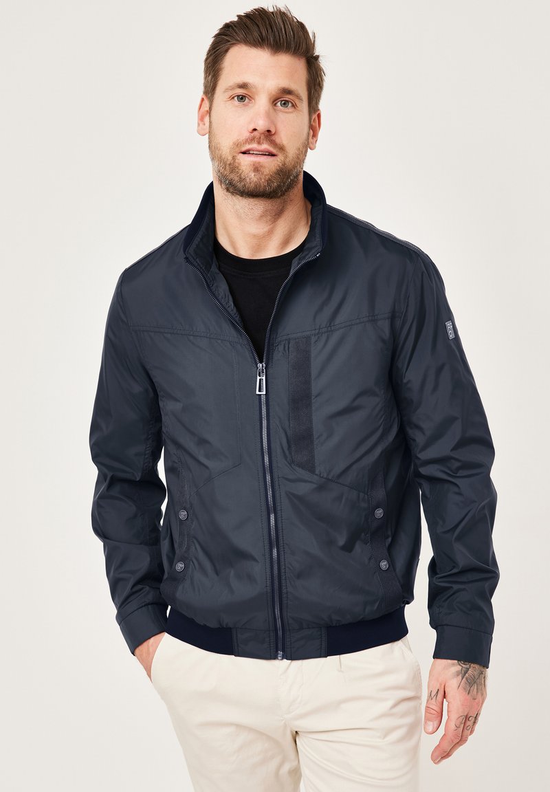 Navy bomber jacket with a zip front, ribbed cuffs, and a textured chest panel. Features side pockets and a lightweight material.