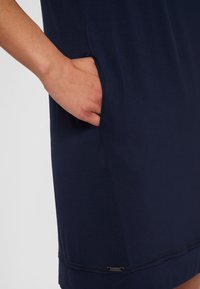 Granatowa sukienka wykonana z miękkiego materiału, z boczną kieszenią i z klasycznie wykończonym dołem, z małą metalową metką logo na dole.