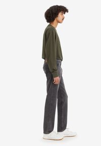 Cămașă verde cu mlaștină lungă, blugi gri drepți, adidași albi. Design simplu, material moale, culori neutre și fără modele vizibile.
