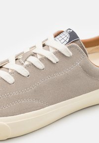 Semišové šedé tenisky s off-white šnúrkami a štruktúrovanou podrážkou. Majú logovú nášivku na jazyku a jemné detaily šitia.