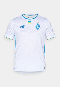 Hvit trøye med teksturert design og blå detaljer, rund krage og New Balance-logo til venstre. Detaljer fra Ukrainas flagg er inkludert.