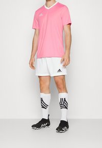 Rosa sporttröja med kort ärm och v-ringning, ihop med vita shorts. Svarta fotbollsskor och knähöga strumpor med svart och vit rand.