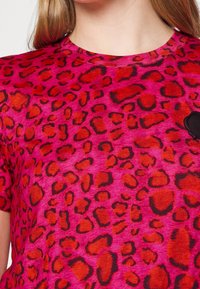 T-shirt fuchsia présentant un motif léopard audacieux en noir et orange, avec un col rond et des manches courtes.